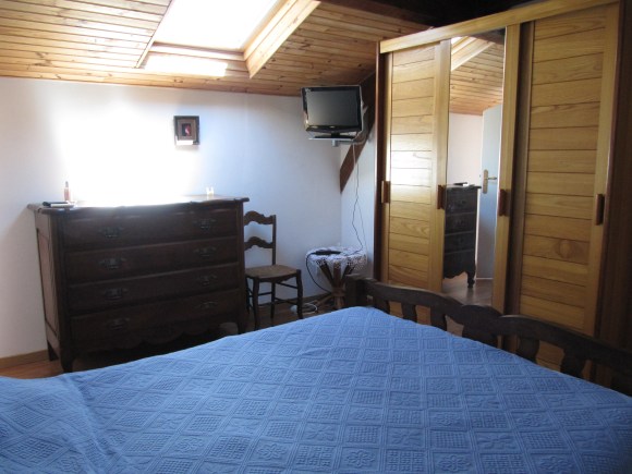 lit avec dessus de lit bleu et velux au deesus d'une vieille commode